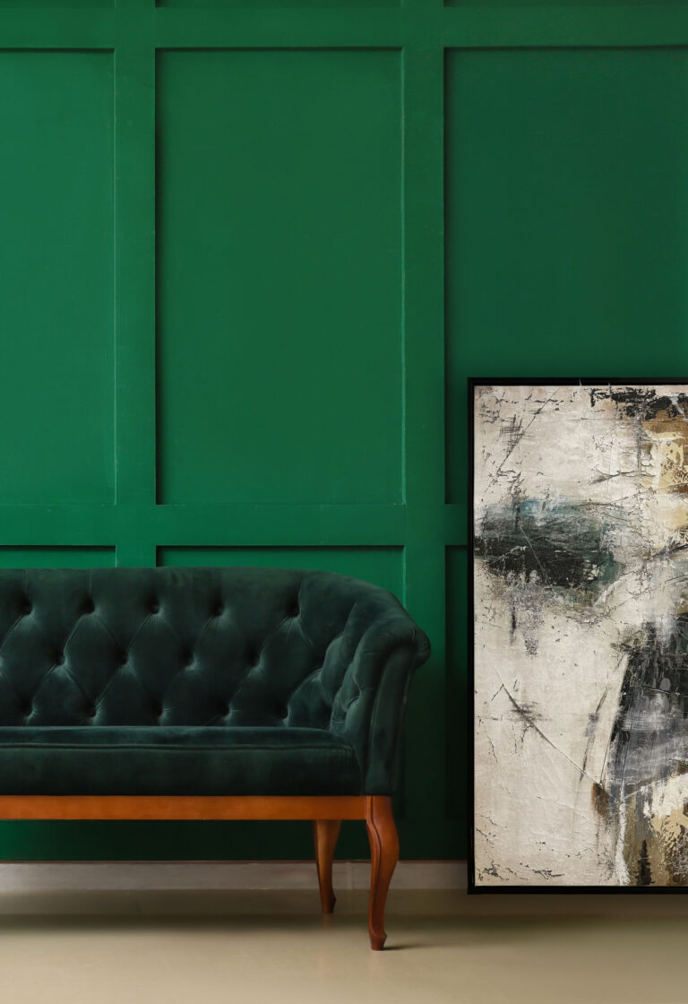 Obraz w stylu nowoczesnym na tle butelkowozielonej ściany, obok welurowej sofy – dekoracja wnętrza w eleganckim stylu