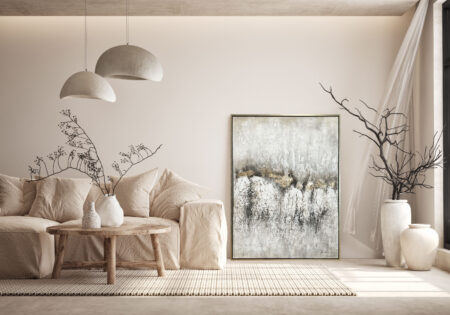 Obraz w naturalnej palecie beżowo-szarej oparty o ścianę w minimalistycznym salonie z lnianą sofą i drewnianym stolikiem